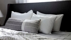 Ein Bett mit dunklem Kopfteil, weißen Kissen und einem grauen, gemusterten Kissen.