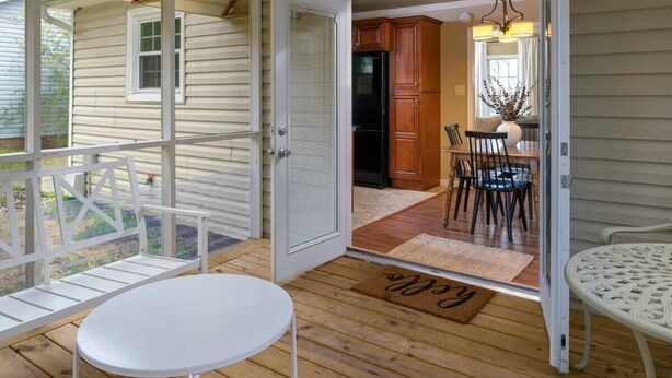 Eine überdachte Veranda mit einem weißen Tisch und Stühlen, eine Tür zu einer Küche mit Holzschränken und einem Kühlschrank.