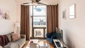 Ein modernes Wohnzimmer mit großem Fenster, Deckenventilator, Sofa, Sessel und Fernseher.