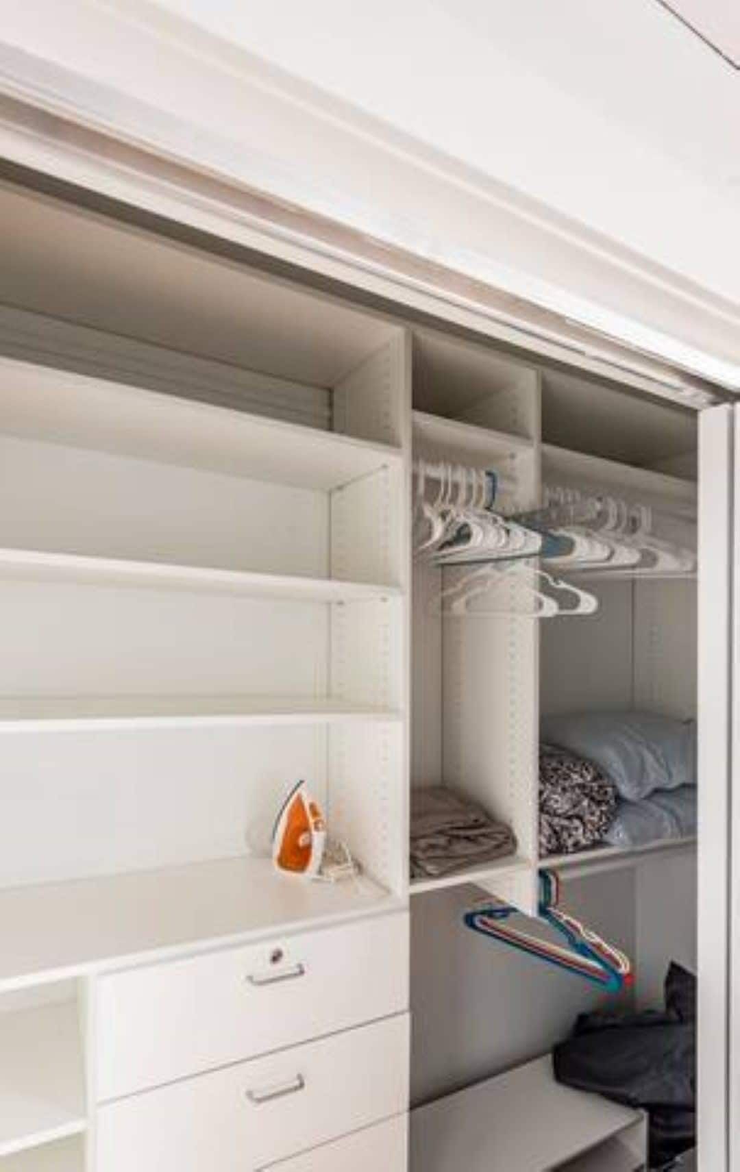 A white closet with open shelves, a hanging rod, and a folded bed.
