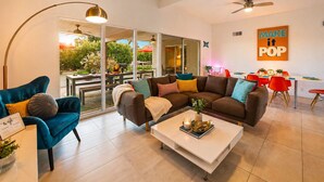 Ein modernes Wohnzimmer mit Sofa, Sessel, Couchtisch und einem Essbereich mit Stühlen und Tisch.