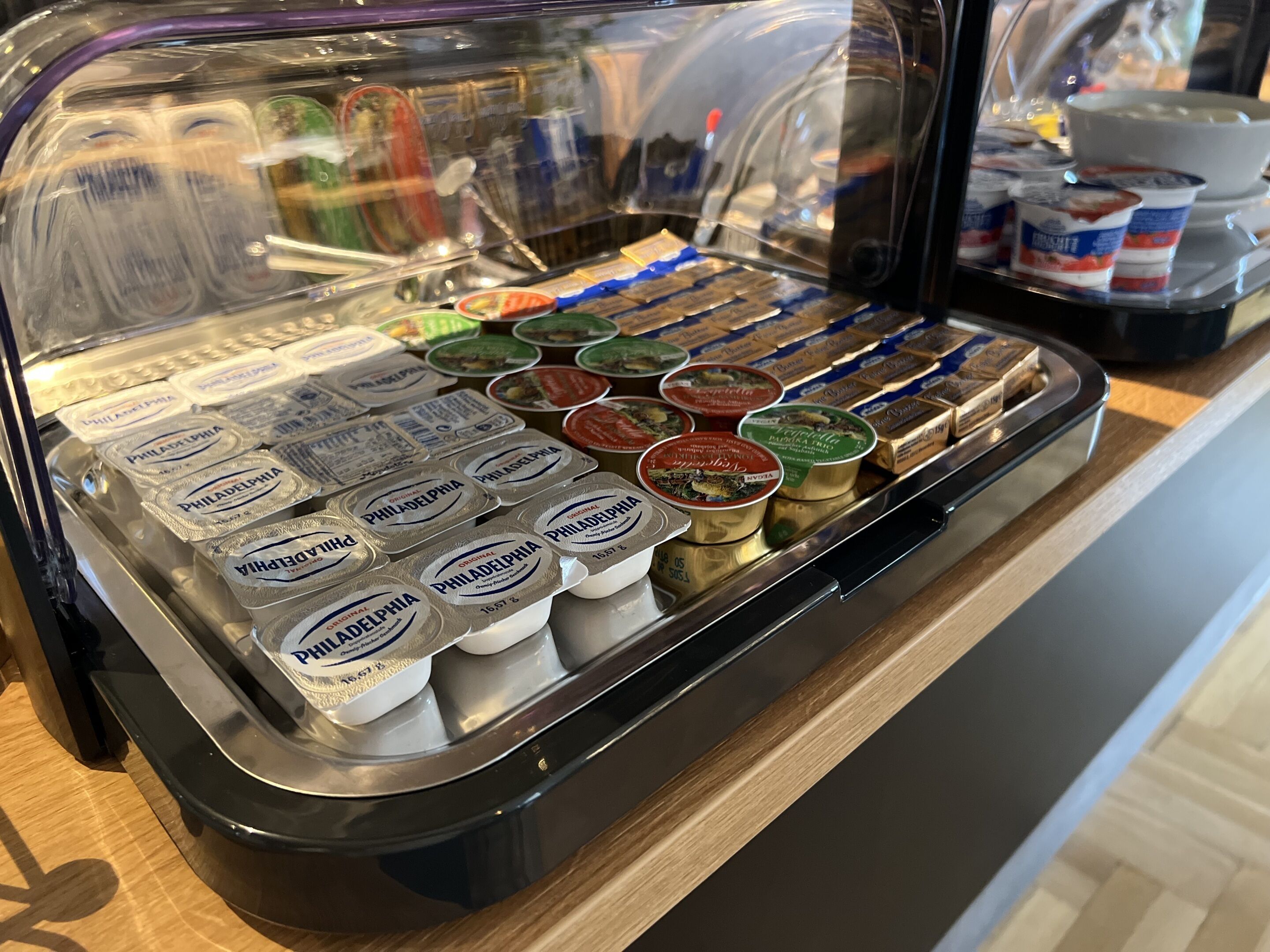 A variety of food items in a display case, including containers of Philadelphia cream cheese and other spreads.