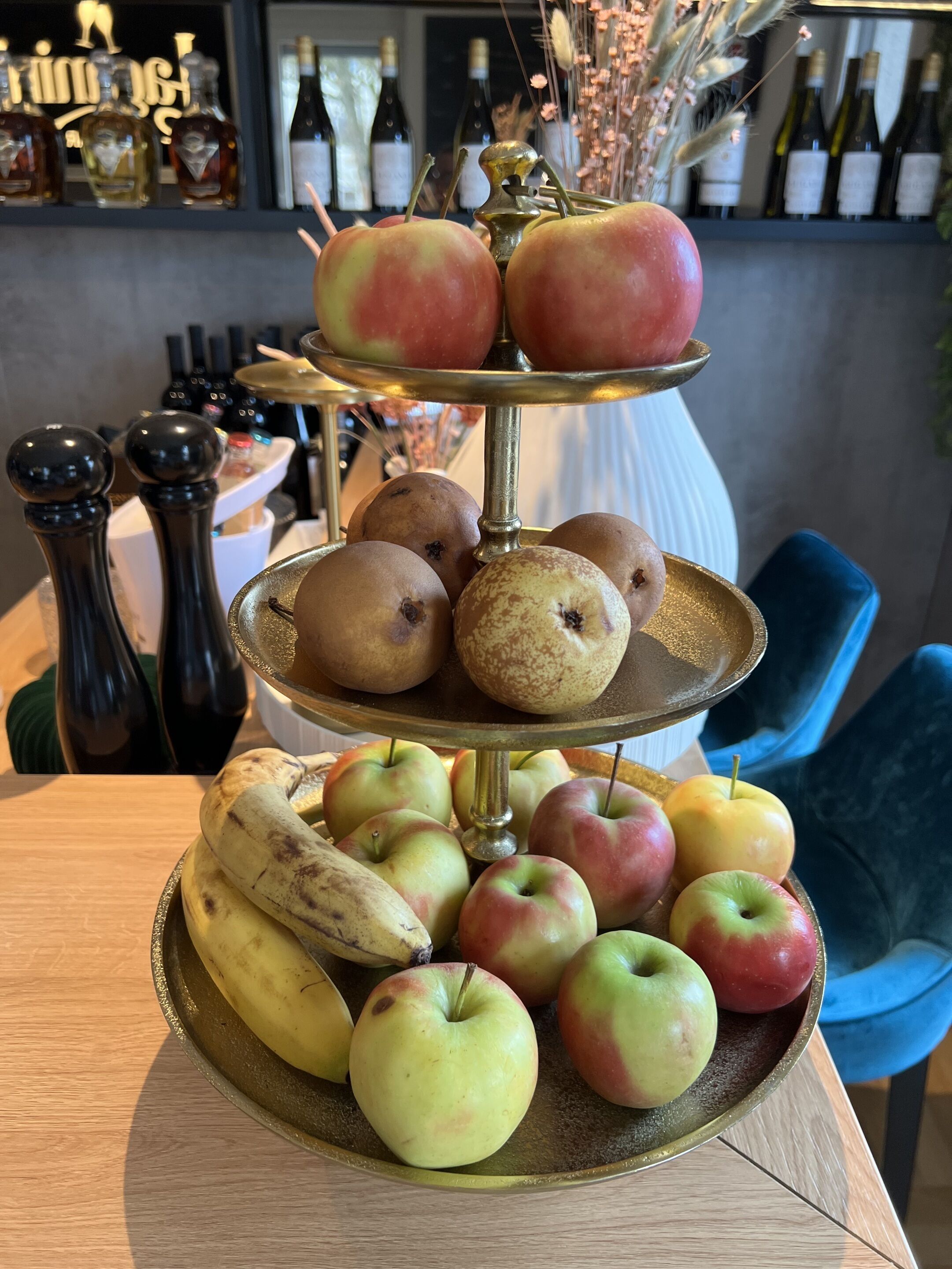 Un puesto de frutas de tres niveles con manzanas y plátanos sobre una mesa de madera en un bar.