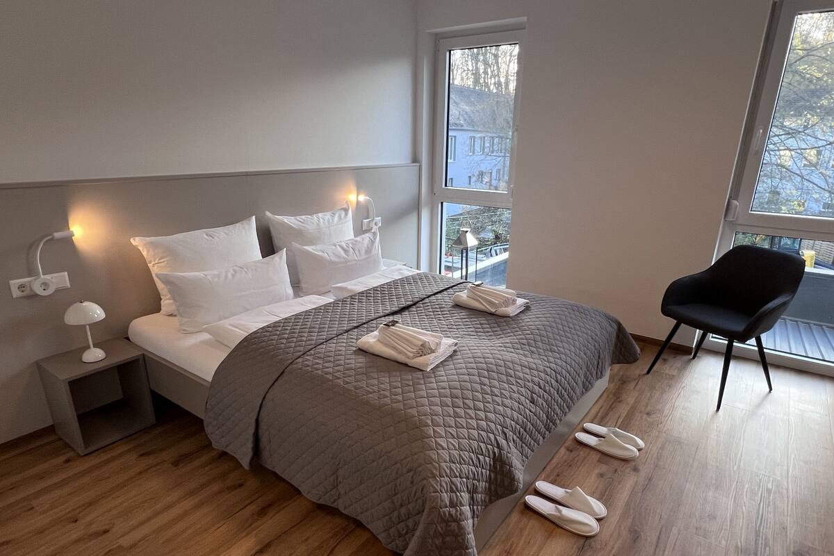 A modern bedroom with a large bed, bedside lamps, a chair, and a view of the outside.