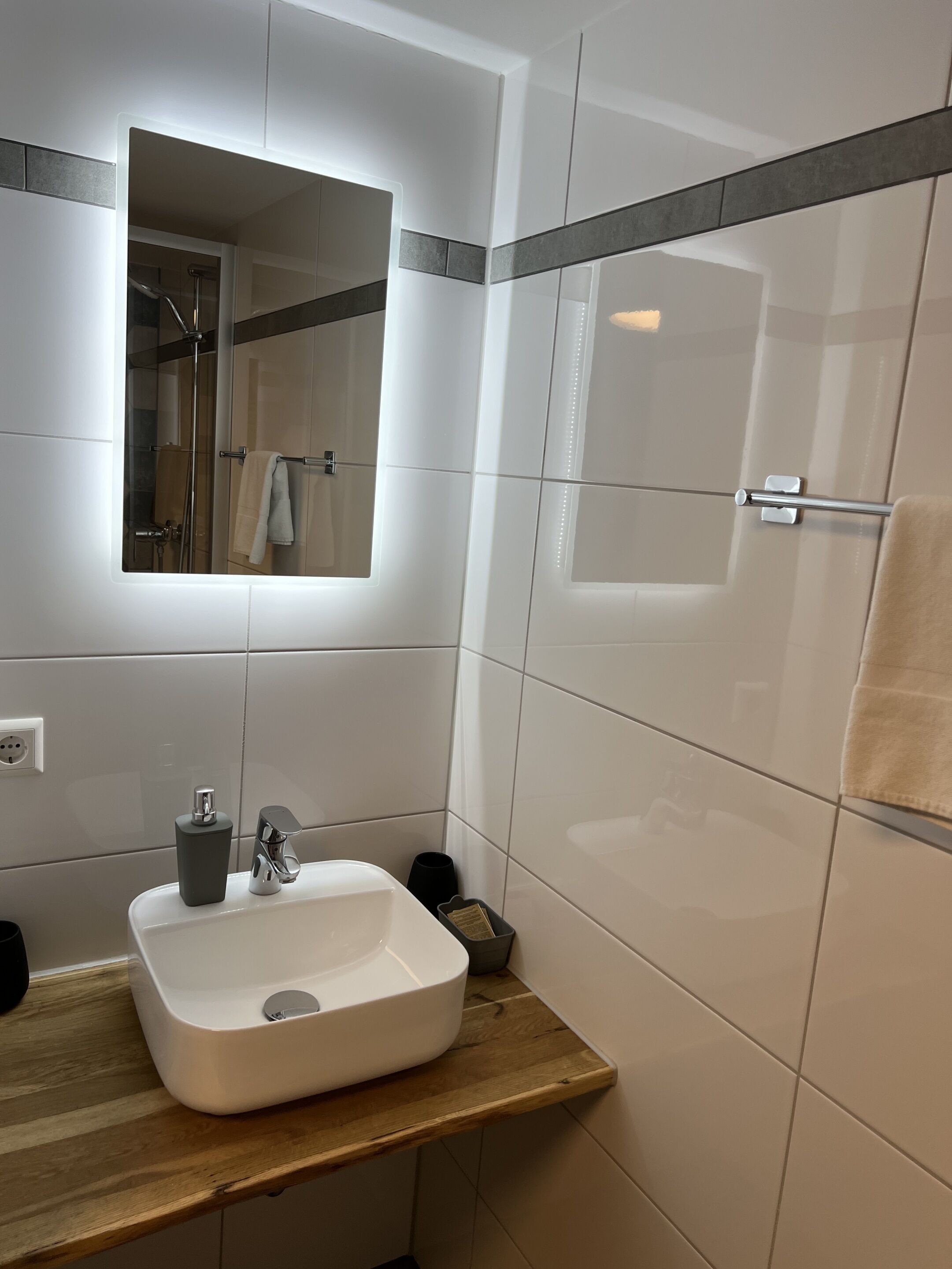 Een moderne badkamer met een witte wastafel, spiegel en douche.