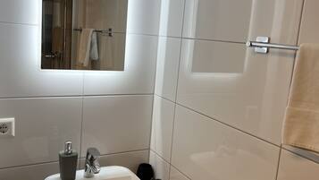 Een moderne badkamer met een witte wastafel, spiegel en douche.