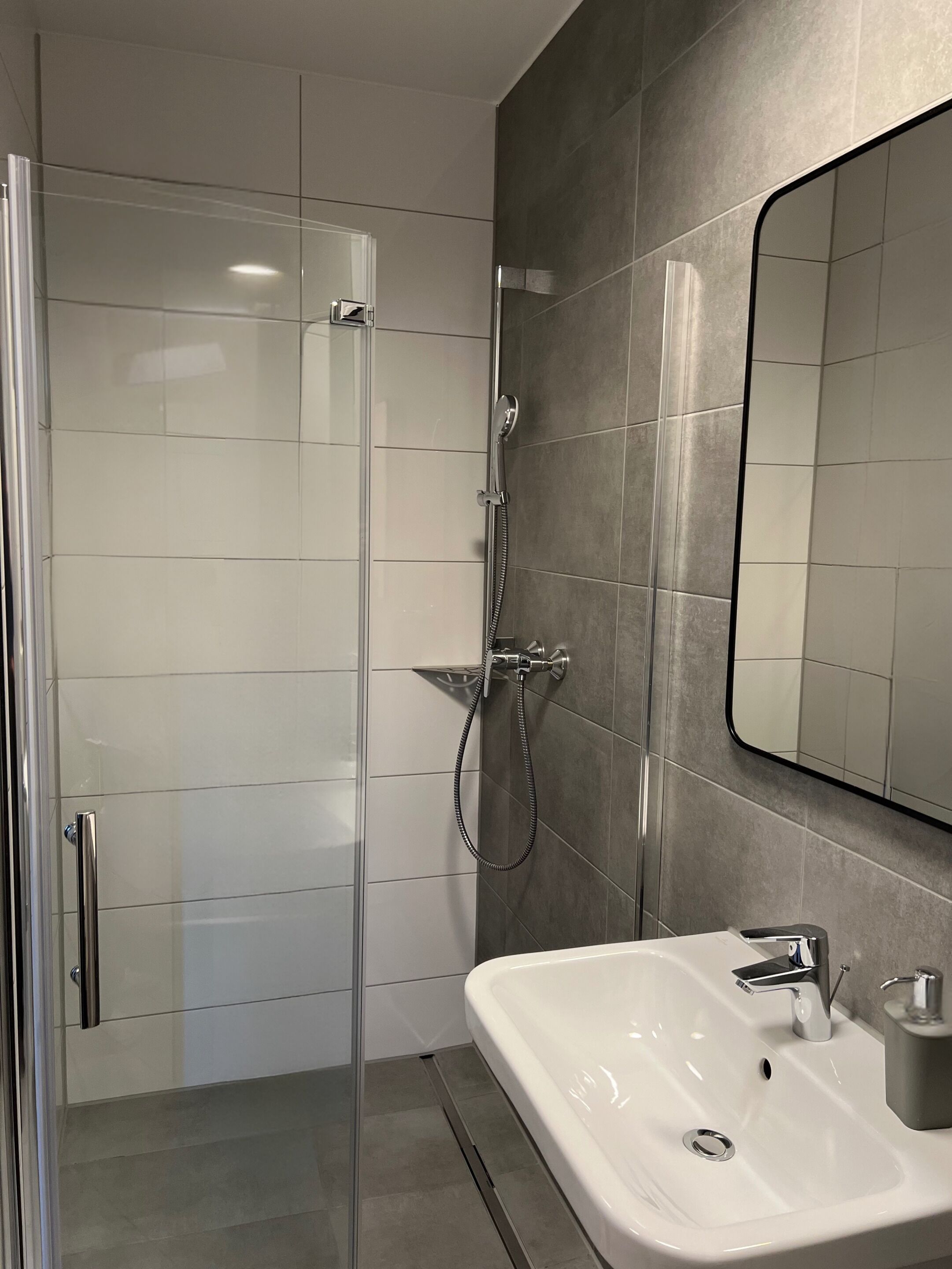 Un baño moderno con ducha de vidrio, un lavamanos blanco con grifo cromado y un espejo grande en la pared.