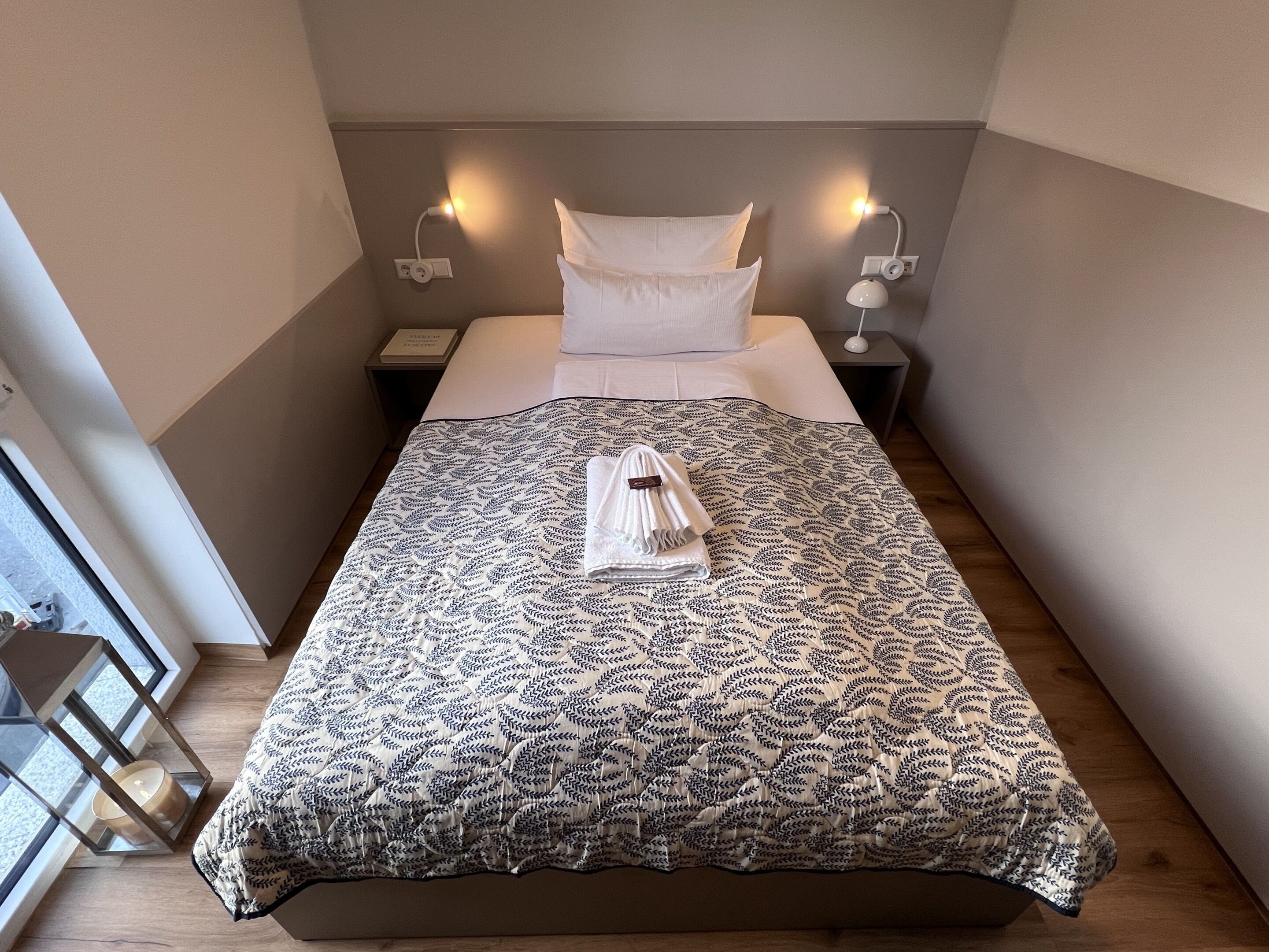 A neatly made bed with a patterned bedspread, two bedside lamps, and a folded towel on the bed.