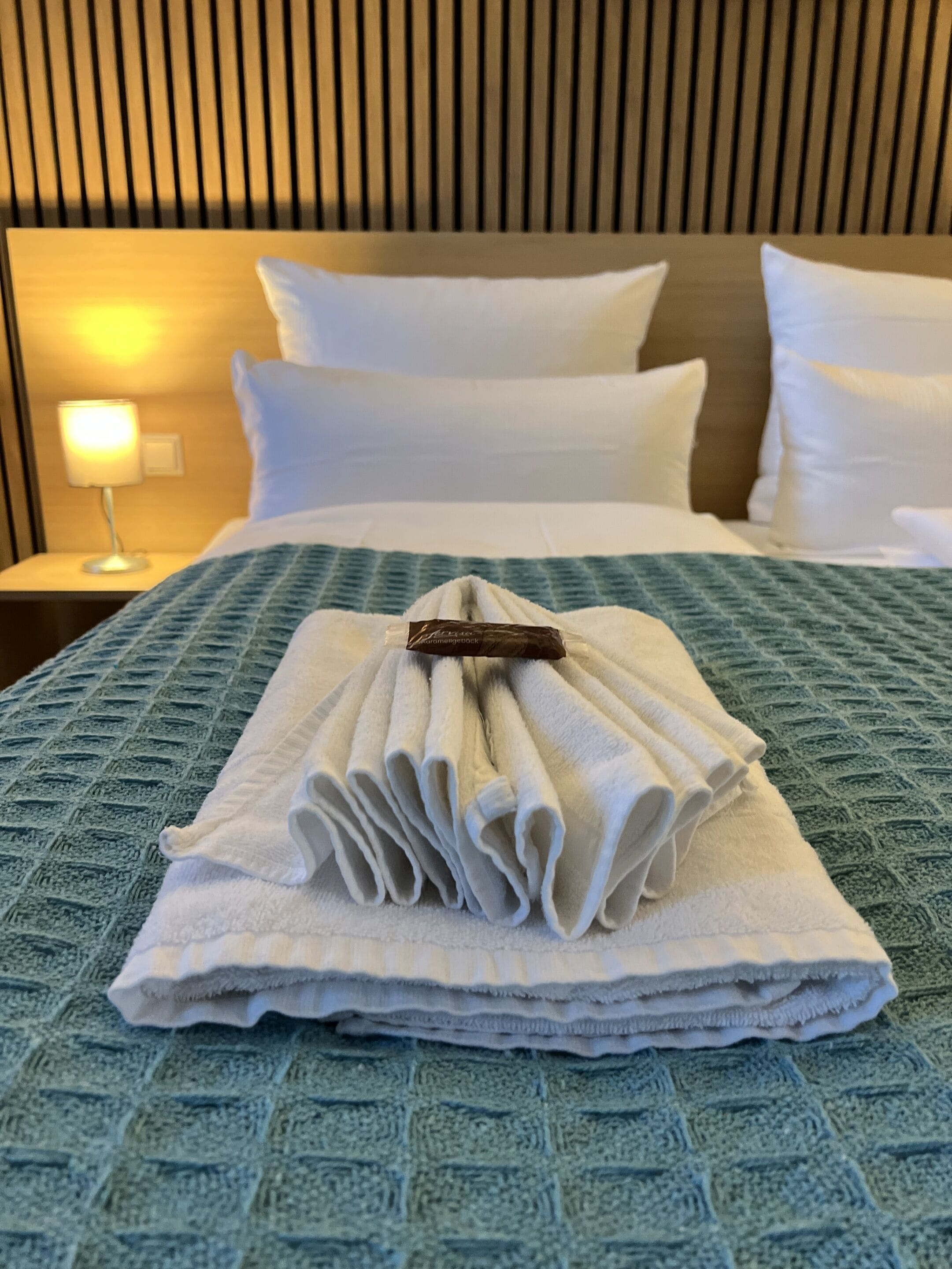A neatly made bed with a folded towel and a small brown item on top, set against a blue textured bedspread.