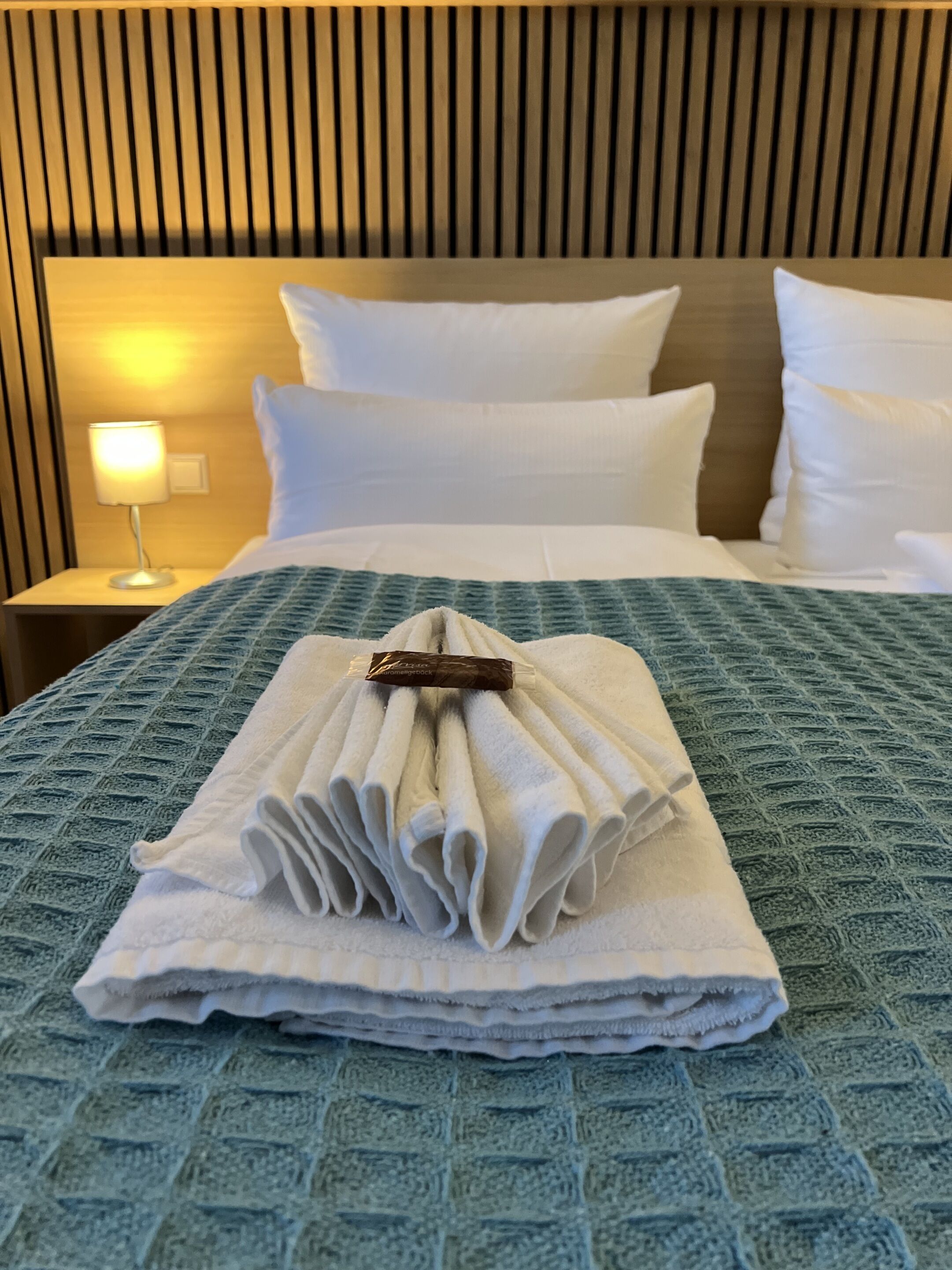 A neatly made bed with a folded towel stack and a pillow on a blue textured bedspread.