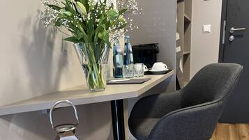 A modern room with a wooden floor, a grey upholstered chair, a small table with a vase of flowers, a candle in a lantern, and a door with a handle.