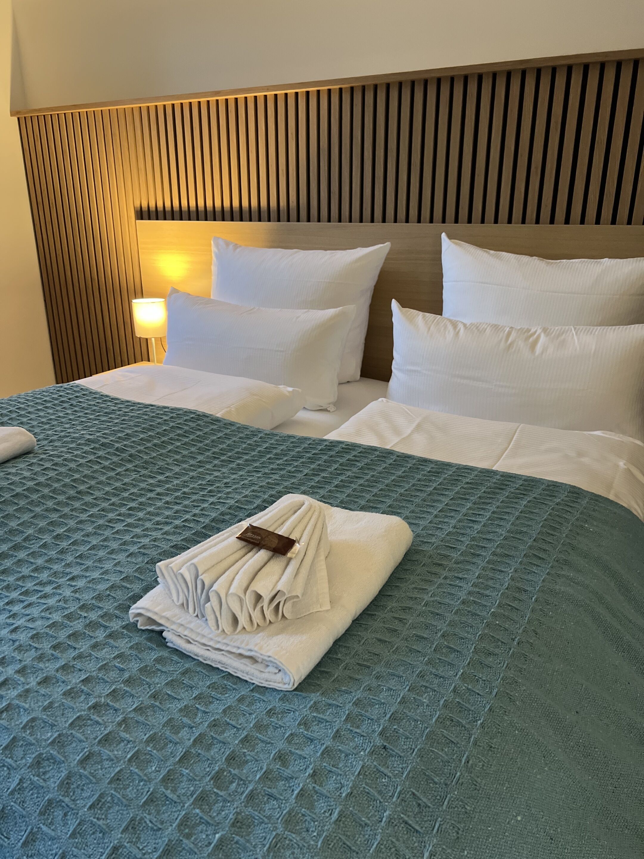 Habitació d'hotel amb un llit gran, un panell de capçalera de fusta i una petita taula de nit amb una làmpada.