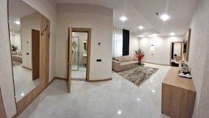 Una habitación de hotel moderna con un espejo grande, un sofá, una mesita de centro y un baño con ducha.