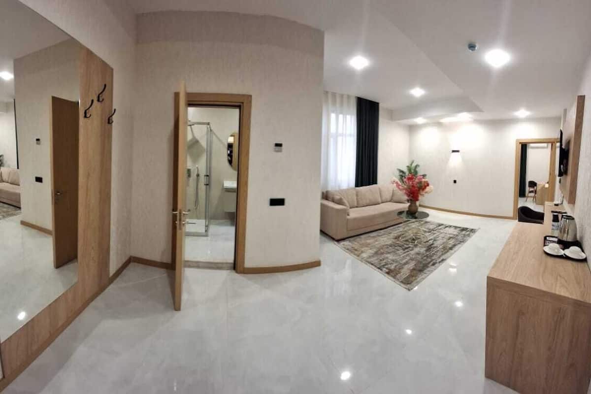 A modern hotel room with a large mirror, a sofa, a coffee table, and a bathroom with a shower.