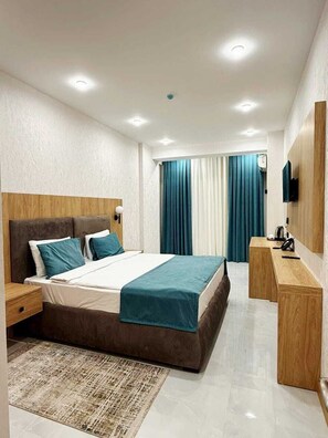 Ett modernt hotellrum med en stor säng, sängbord, ett skrivbord, en platt-TV och ett fönster med gardiner.