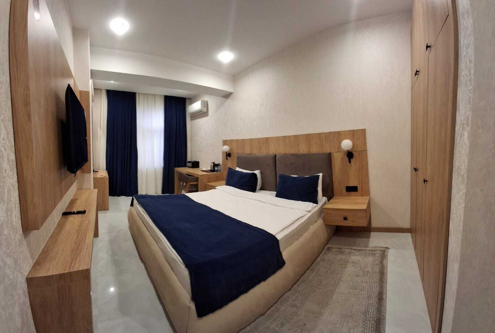 A modern hotel room with a large bed, bedside tables, a desk, and a TV mounted on the wall.