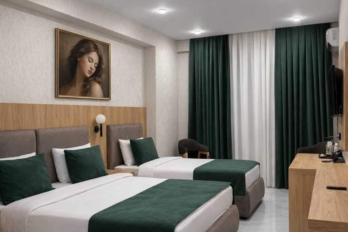 A modern hotel room with two beds, a desk, a chair, and a painting on the wall.
