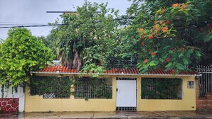 A yellow building with a tiled roof, a white door, and a barred window. - Casa Seloria (Cancún)