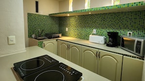 A kitchen with a black induction cooktop, a microwave, and a toaster. There are cabinets with a green-tiled backsplash. - Casa Seloria (Cancún)
