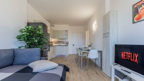 Een modern appartement met een bank, een eethoek, een keuken en een televisie waarop 'NETFLIX' wordt getoond.