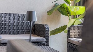 Een rieten bank met een kussen en een lamp, geplaatst naast een grote groene plant.