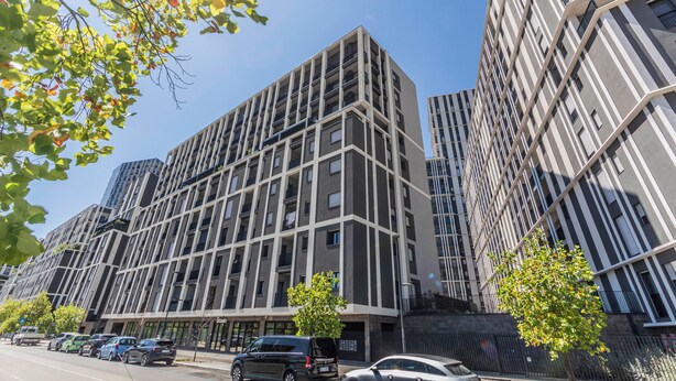 Een modern meerhoogbouwgebouw met een rastergevel, grote ramen en een parkeerplaats met meerdere auto's.