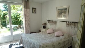 A bedroom with a bed, a nightstand, a chair, a window with curtains, and a view of the outdoors. - Le Verger du Sausset (Beaune)