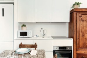 A kitchen with white cabinets, a microwave, a sink, a wooden chair, and an oven. - Villa Eugenia Suite 2 - MyHomeinComo (Carate Urio)