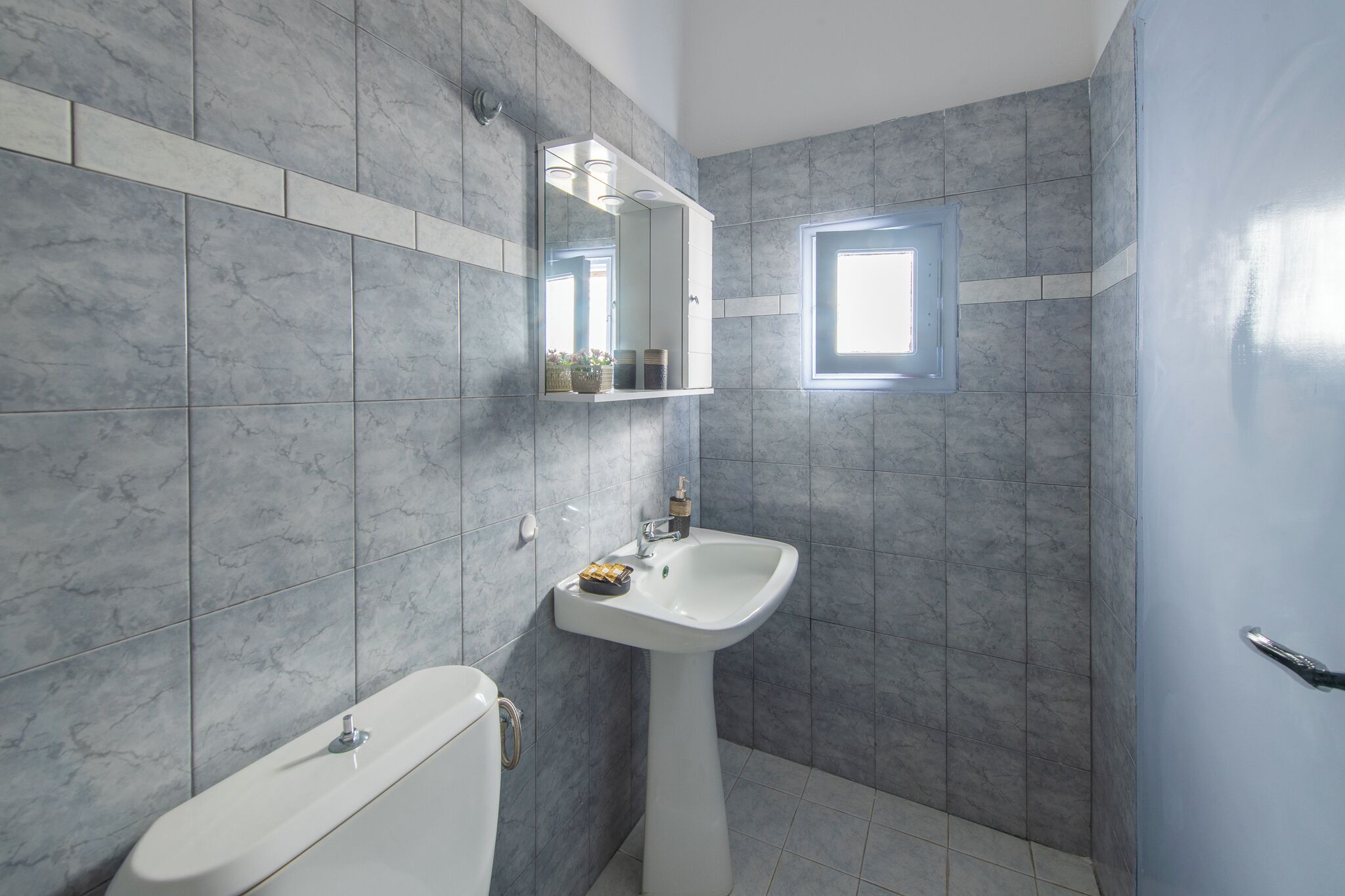 A bathroom with a white pedestal sink, a mirror, and a window.