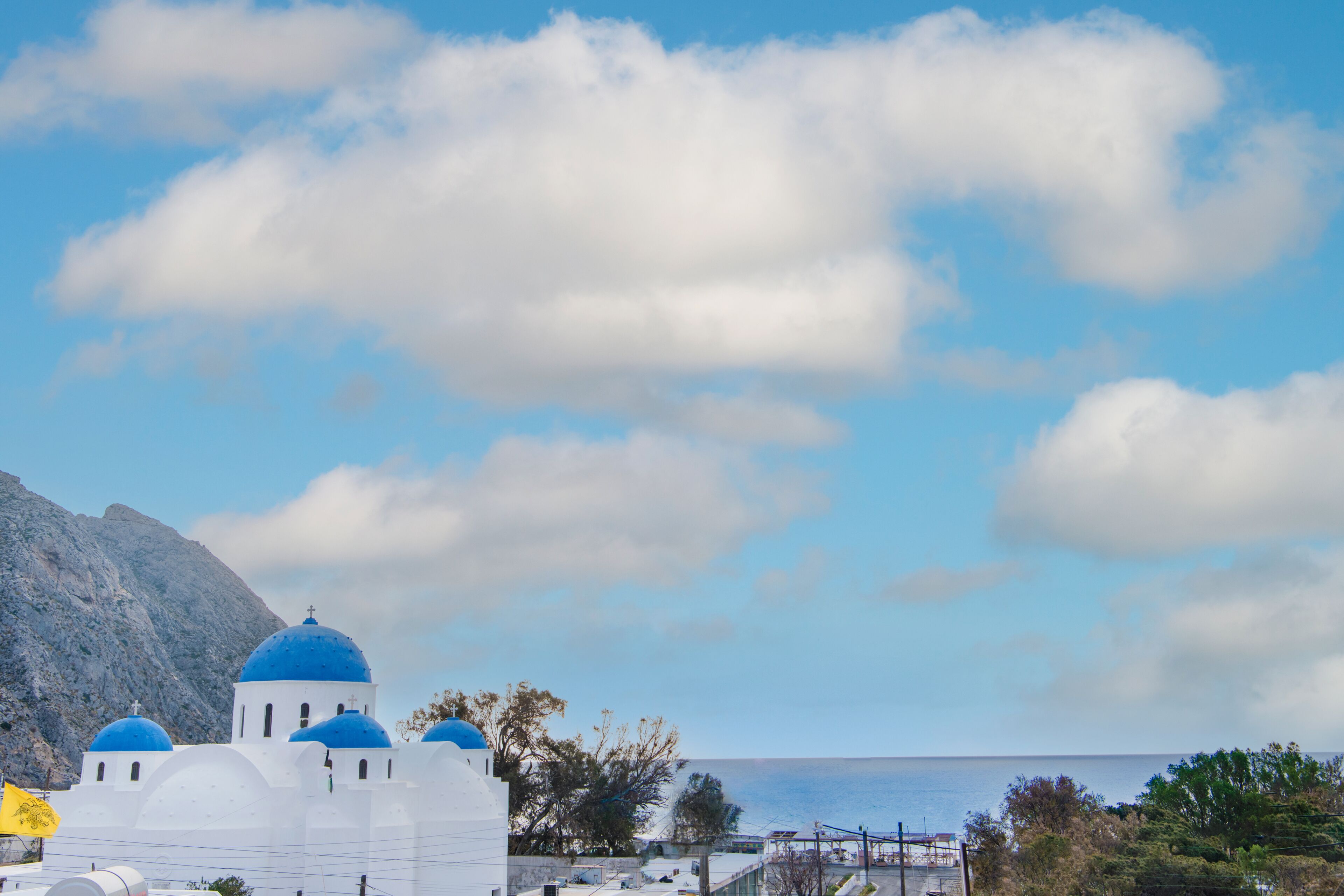 A coastal building with blue domes, a mountain in the background, and a clear sky.