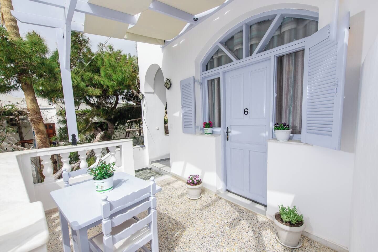 A white exterior with a door marked '6', a small table with chairs, and potted plants.