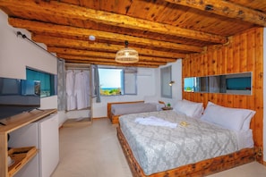 Un dormitorio con techo de madera, una cama con colcha estampada, una mesita de noche con lámpara y una ventana con vistas.