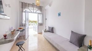 Quarto com cama, uma pequena mesa, uma cadeira, janela com cortinas e ar condicionado.