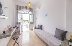 Una habitación con cama, una mesita, una silla, ventana con cortinas y un equipo de aire acondicionado.