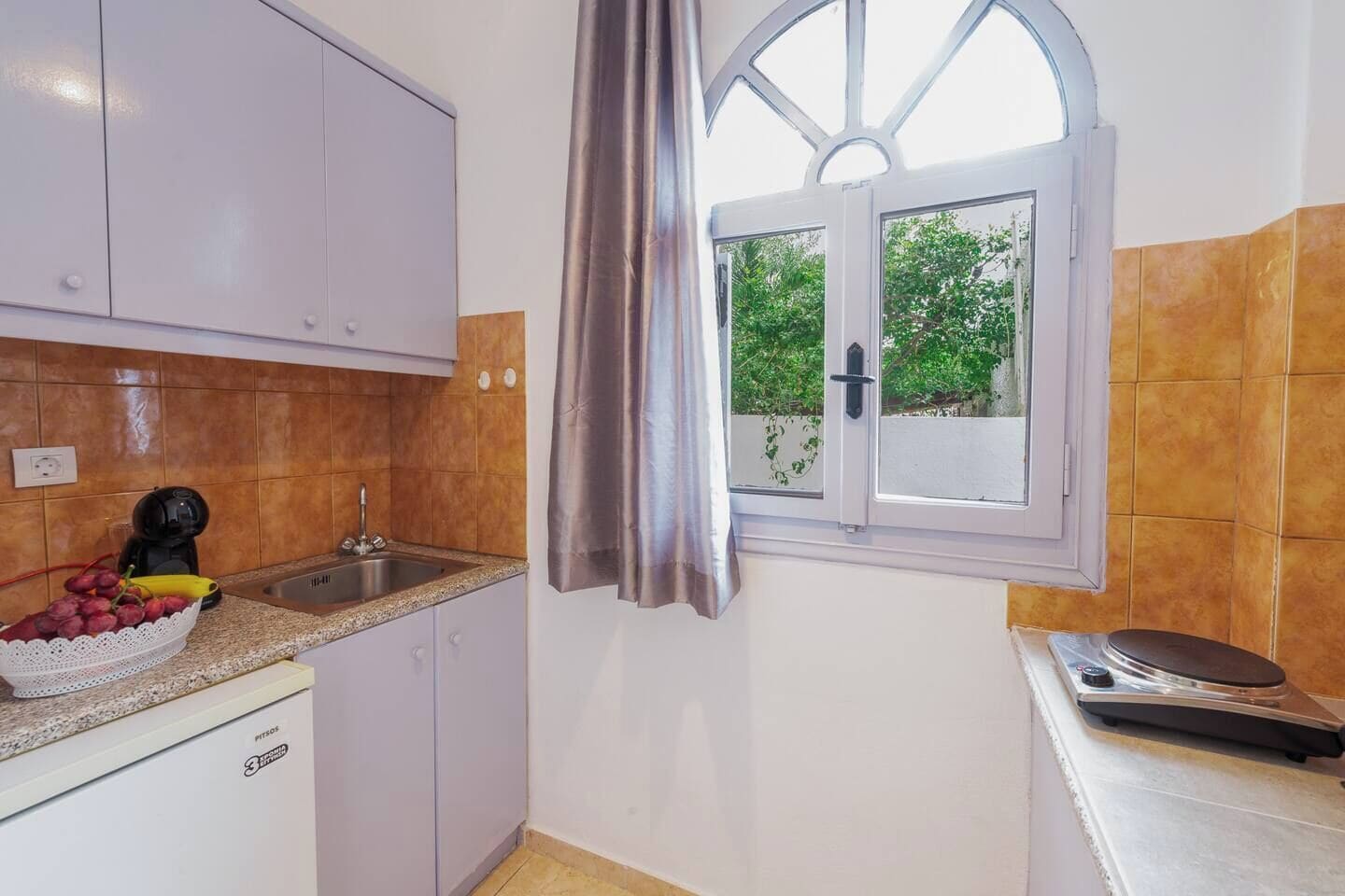 A kitchen with a sink, a fruit bowl, a coffee machine, and a window with curtains.
