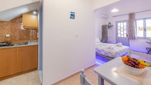 Quarto compacto com cozinha compacta, uma cama com colcha branca e uma mesa com uma fruteira.