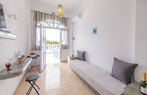 Habitación pequeña con cama, una mesita, una silla, kitchenette y vistas al exterior.