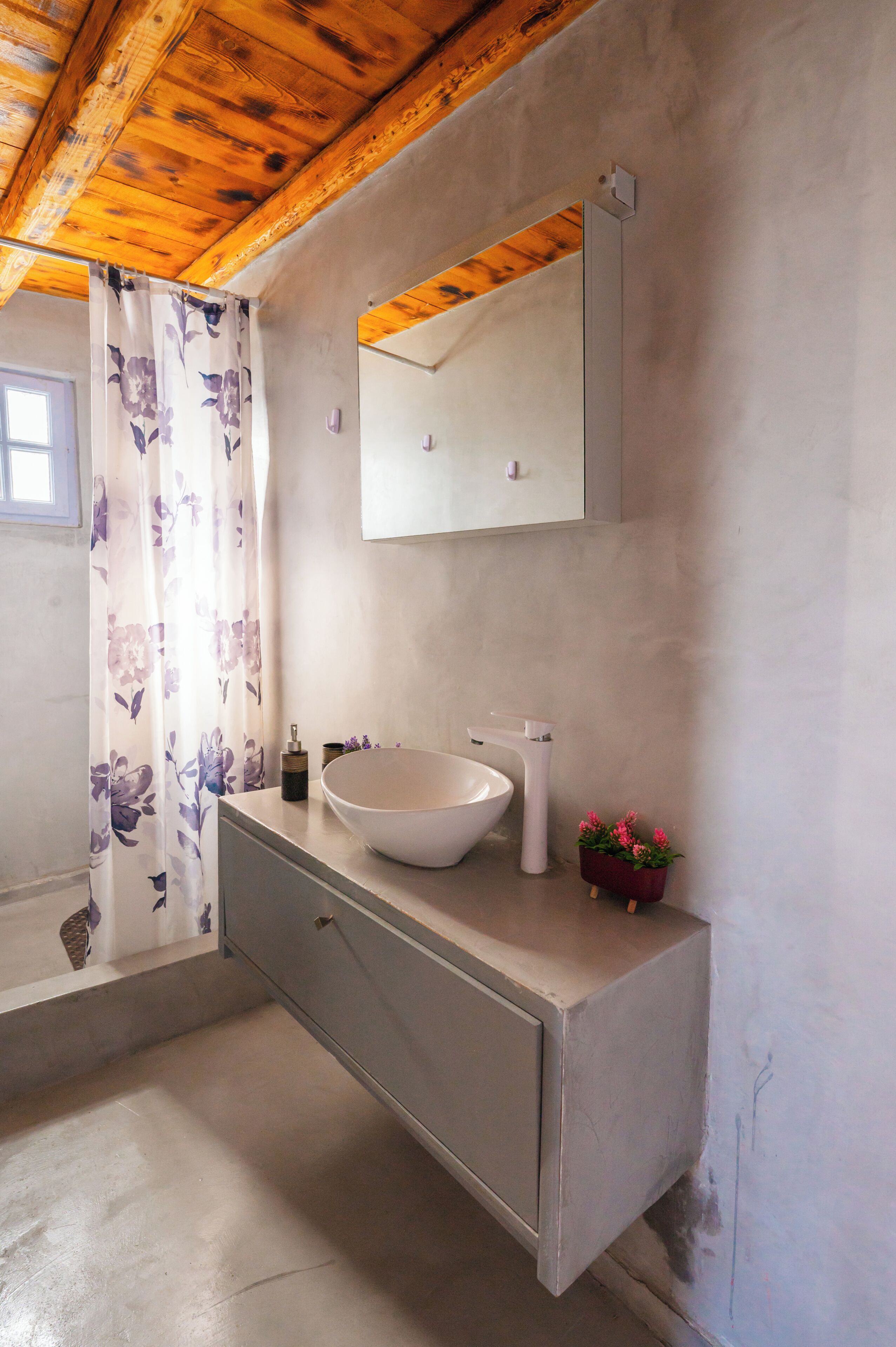 A bathroom with a wooden ceiling, a large white sink, a mirror, and a floral shower curtain.