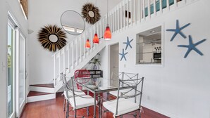Een moderne eetruimte met een glazen tafel, metalen stoelen, witte muren en decoratieve muurkunst in de vorm van zeesterren.