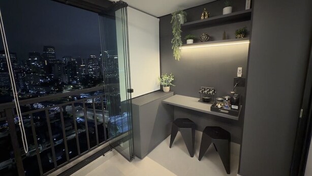 Uma varanda moderna com vista para a cidade, uma mesa pequena com bancos e uma estante com objetos decorativos.