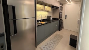 Uma cozinha moderna com geladeira de aço inoxidável, armários cinzas, bancada preta, pia, micro-ondas e máquina de lavar.