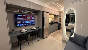 Uma cozinha moderna com televisão integrada, área de jantar com duas cadeiras e um sofá na sala de estar.