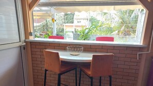 A small dining area with a round table and two chairs, a window with a view of the outside, and a basket on the table. - Lovely apartment with private pool - Rivière-Pilote (Martinique) (Rivière-Pilote)
