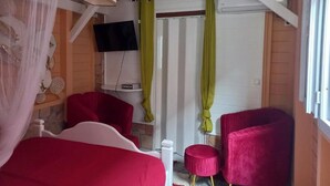 A room with a bed, a red chair, a small round table, a television, and a window with curtains. - Lovely apartment with private pool - Rivière-Pilote (Martinique) (Rivière-Pilote)