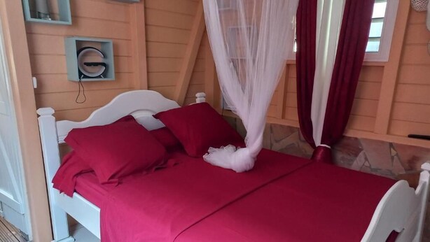 A bed with a red bedspread and white headboard in a room with wooden walls and a sloped ceiling. - Lovely apartment with private pool - Rivière-Pilote (Martinique) (Rivière-Pilote)