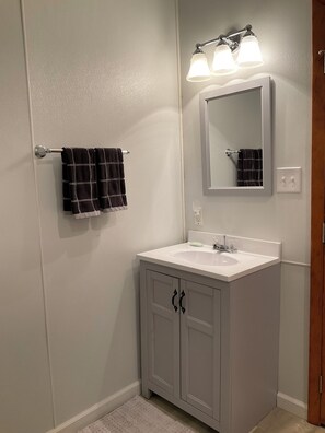 A bathroom with a white sink, a mirror, and a towel rack with a black towel.