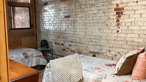 Een kamer met twee bedden, een houten dressoir en een bakstenen muur.