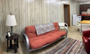 A compact living space with a sofa, a small table, a lamp, and a kitchen area in the background.