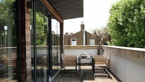 A modern balcony with glass doors, wicker furniture, and a view of a brick building. - The Westview: 2BR Penthouse &Terrace in White City (London)