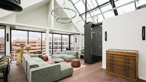 Un loft spacieux avec un plafond haut, de grandes fenêtres offrant une vue sur la ville, un canapé d’angle, une commode en bois et un lustre.